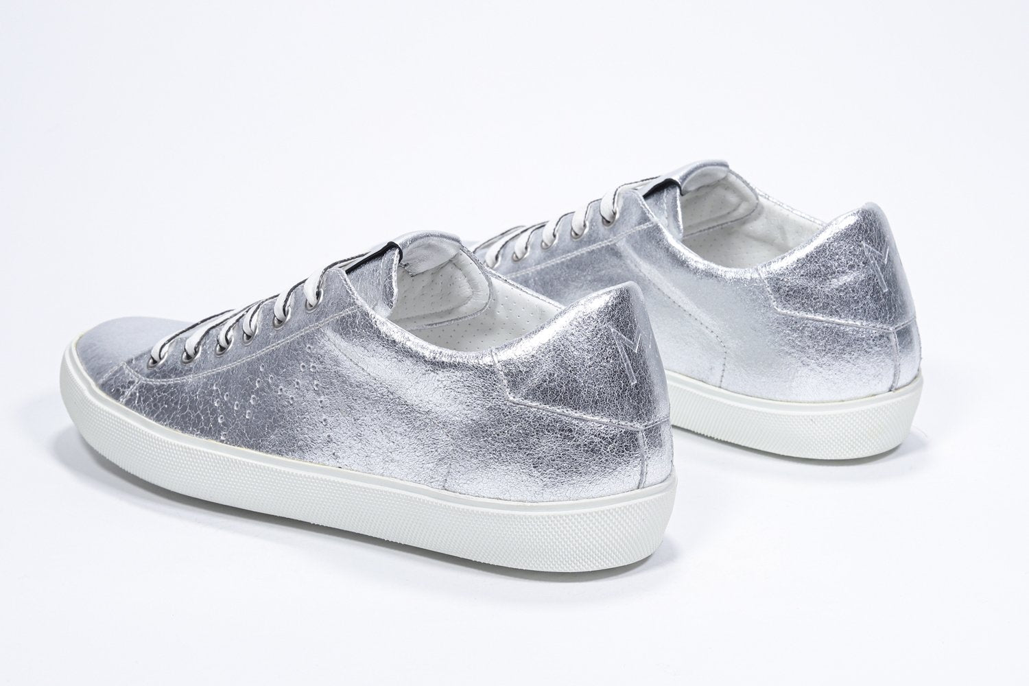 Three quarter back view of low top silver sneaker with perforated crown logo on upper. Full metallic leather upper and white rubber sole.