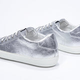 Dreiviertelansicht der Rückseite des silbernen Low Top sneaker mit perforiertem Kronenlogo auf dem Obermaterial. Obermaterial aus Metallic-Leder und weiße Gummisohle.