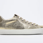 Side profile of low top gold sneaker with perforated crown logo on upper. Full metallic leather upper and white rubber sole.