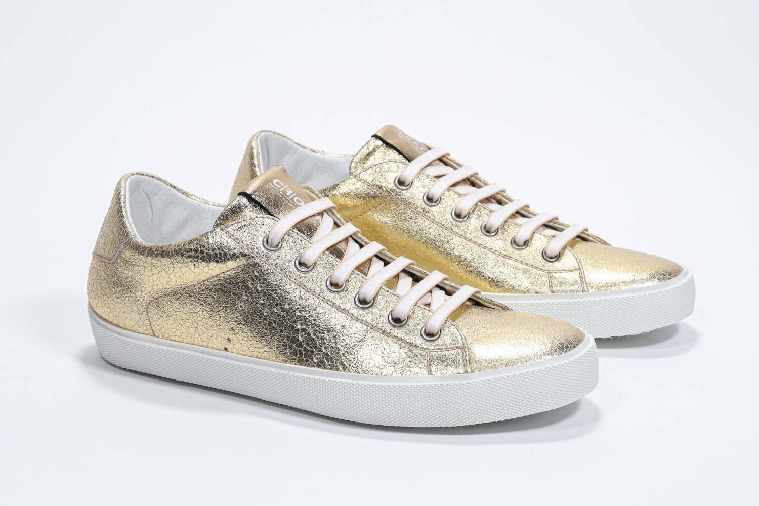 Three quarter front view of low top gold sneaker with perforated crown logo on upper. Full metallic leather upper and white rubber sole.