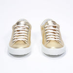 Front view of low top gold sneaker with perforated crown logo on upper. Full metallic leather upper and white rubber sole.
