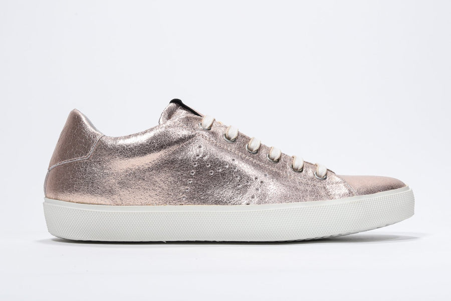 Side profile of low top rose-gold sneaker with perforated crown logo on upper. Full metallic leather upper and white rubber sole.