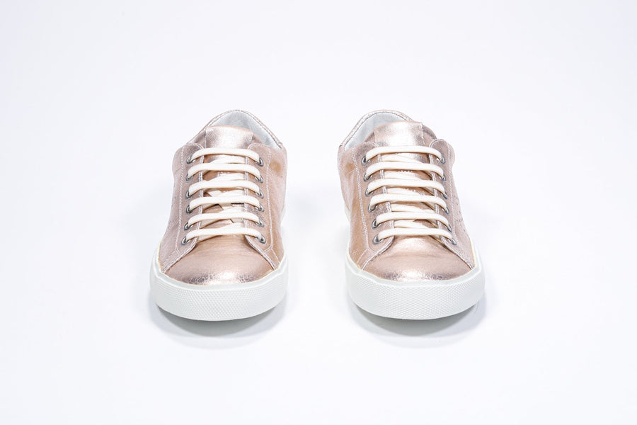 Front view of low top rose-gold sneaker with perforated crown logo on upper. Full metallic leather upper and white rubber sole.