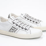 Three quarter front view of low top white sneaker. Full leather upper with studs and vintage rubber sole.