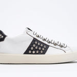 Side profile of low top white and black sneaker. Full leather upper with studs and vintage rubber sole.