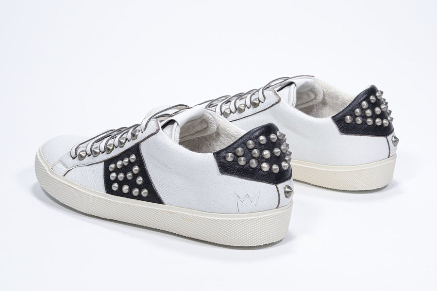 Three quarter back view of low top white and black sneaker. Full leather upper with studs and vintage rubber sole.