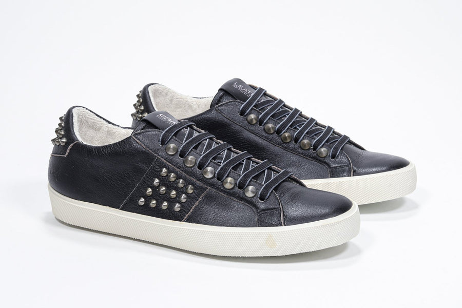 Three quarter front view of low top black sneaker. Full leather upper with studs and antique rubber sole.