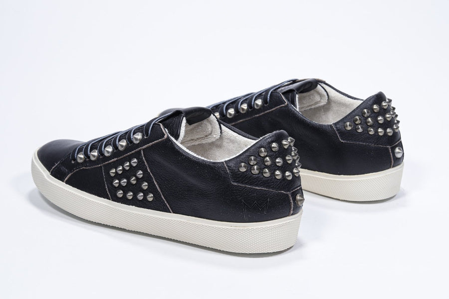 Three quarter back view of low top black sneaker. Full leather upper with studs and antique rubber sole.
