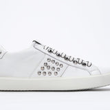 Side profile of low top white sneaker. Full leather upper with studs and white rubber sole.