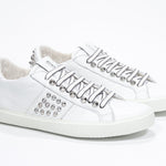 Three quarter front view of low top white sneaker. Full leather upper with studs and white rubber sole.