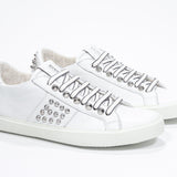 Three quarter front view of low top white sneaker. Full leather upper with studs and white rubber sole.