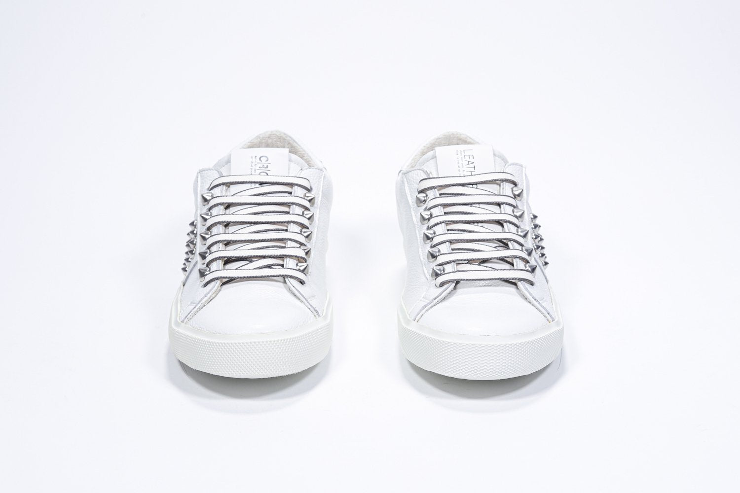 Vue de face de la chaussure blanche sneaker. Tige en cuir avec clous et semelle en caoutchouc blanc.