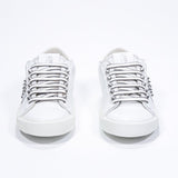 Front view of low top white sneaker. Full leather upper with studs and white rubber sole.
