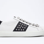 Profil latéral d'un bas blanc et noir sneaker. Tige en cuir avec clous et semelle en caoutchouc blanc.