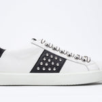 Side profile of low top white and black sneaker. Full leather upper with studs and white rubber sole.