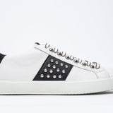 Side profile of low top white and black sneaker. Full leather upper with studs and white rubber sole.