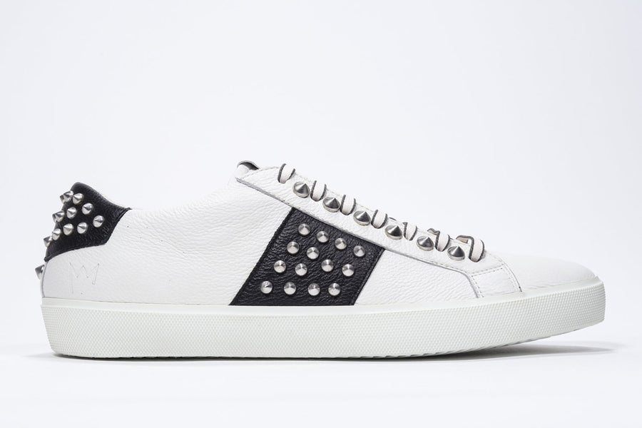 Side profile of low top white and black sneaker. Full leather upper with studs and white rubber sole.