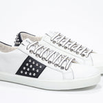 Three quarter front view of low top white and black sneaker. Full leather upper with studs and white rubber sole.
