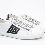 Three quarter front view of low top white and black sneaker. Full leather upper with studs and white rubber sole.