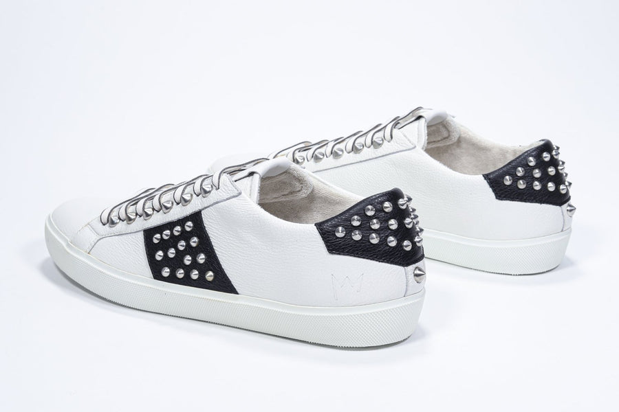 Three quarter back view of low top white and black sneaker. Full leather upper with studs and white rubber sole.