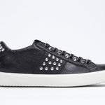 Side profile of low top black sneaker. Full leather upper with studs and white rubber sole.