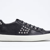 Side profile of low top black sneaker. Full leather upper with studs and white rubber sole.