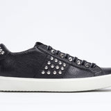 Profilo laterale di BASSE nero sneaker. Tomaia in pelle con borchie e suola in gomma bianca.