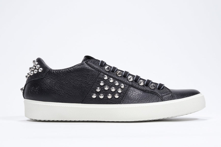 Side profile of low top black sneaker. Full leather upper with studs and white rubber sole.