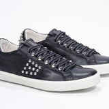 Tre quarti di BASSE nero sneaker. Tomaia in pelle con borchie e suola in gomma bianca.