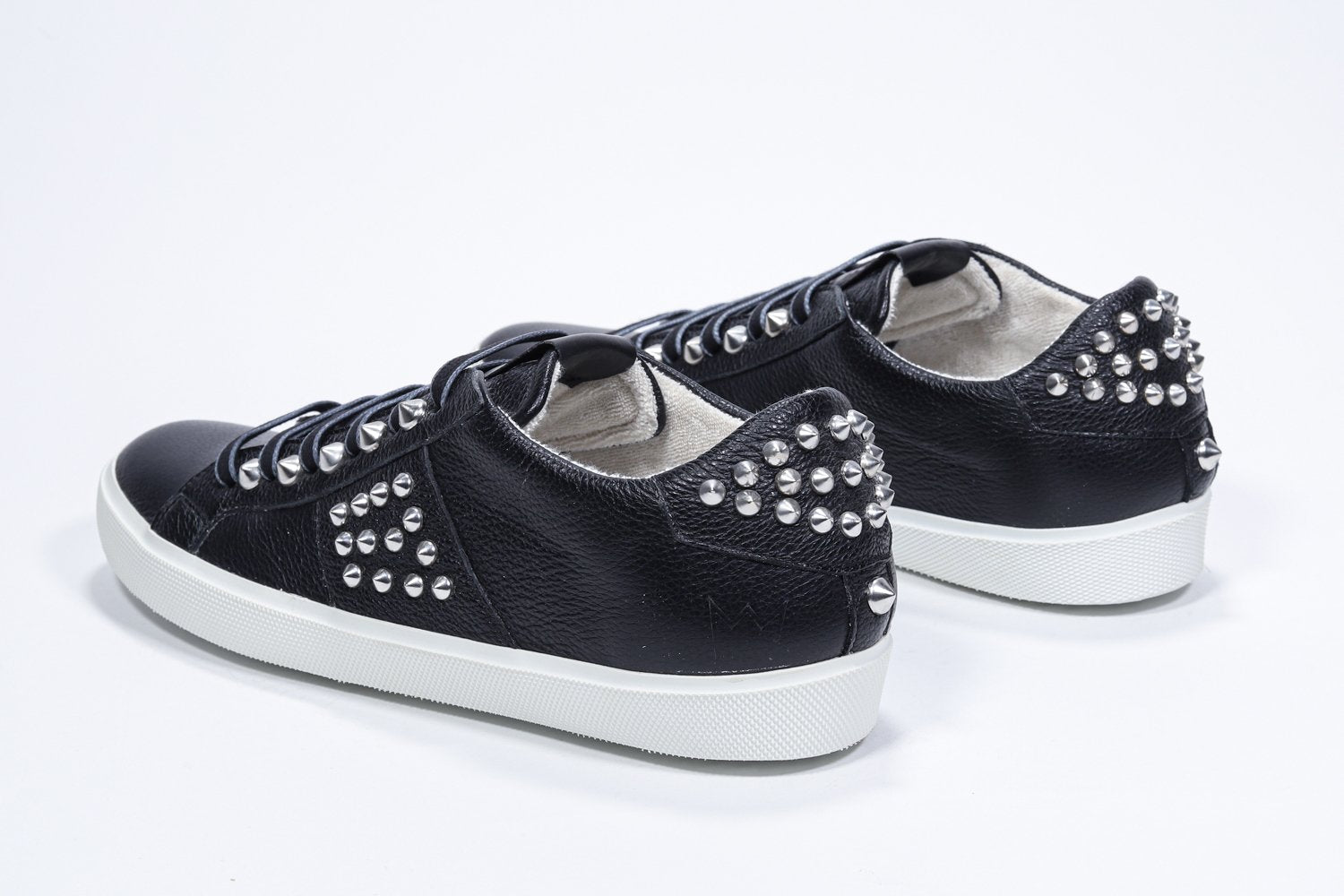 Three quarter back view of low top black sneaker. Full leather upper with studs and white rubber sole.