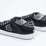 Three quarter back view of low top black sneaker. Full leather upper with studs and white rubber sole.