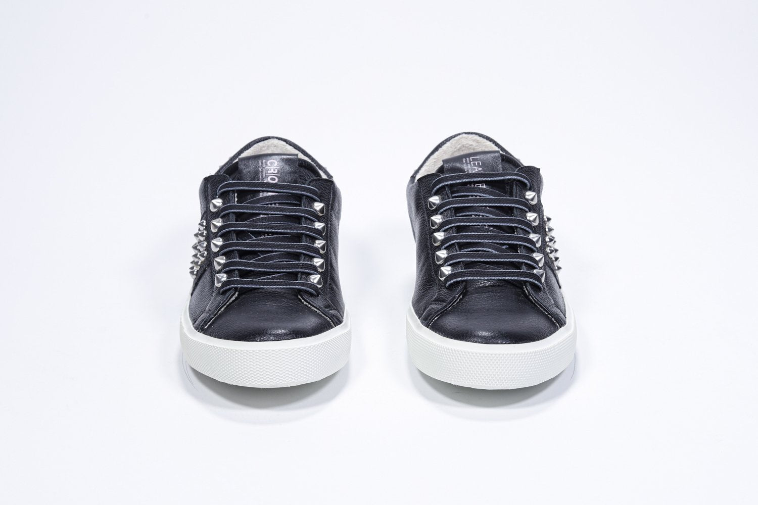 Vue de face de la chaussure noire sneaker. Tige en cuir avec clous et semelle en caoutchouc blanc.