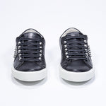 Front view of low top black sneaker. Full leather upper with studs and white rubber sole.
