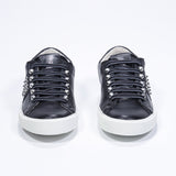 Vue de face de la chaussure noire sneaker. Tige en cuir avec clous et semelle en caoutchouc blanc.
