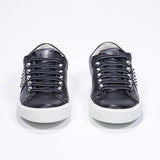 Front view of low top black sneaker. Full leather upper with studs and white rubber sole.