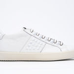 Side profile of low top white sneaker. Full leather upper with studs and vintage rubber sole.