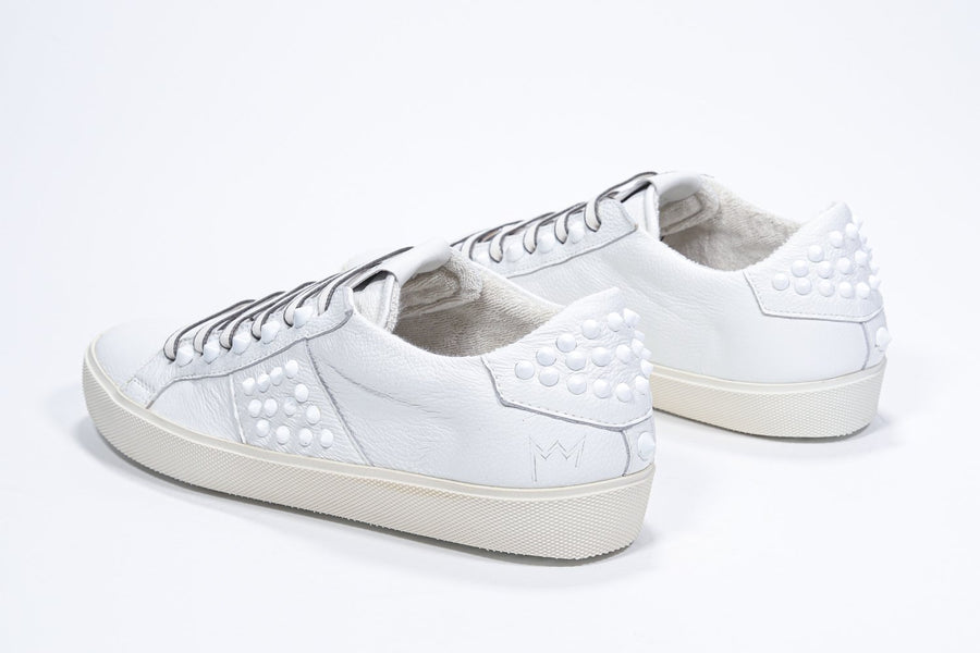 Three quarter back view of low top white sneaker. Full leather upper with studs and vintage rubber sole.