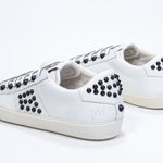 Three quarter back view of low top white sneaker. Full leather upper with studs and vintage rubber sole.