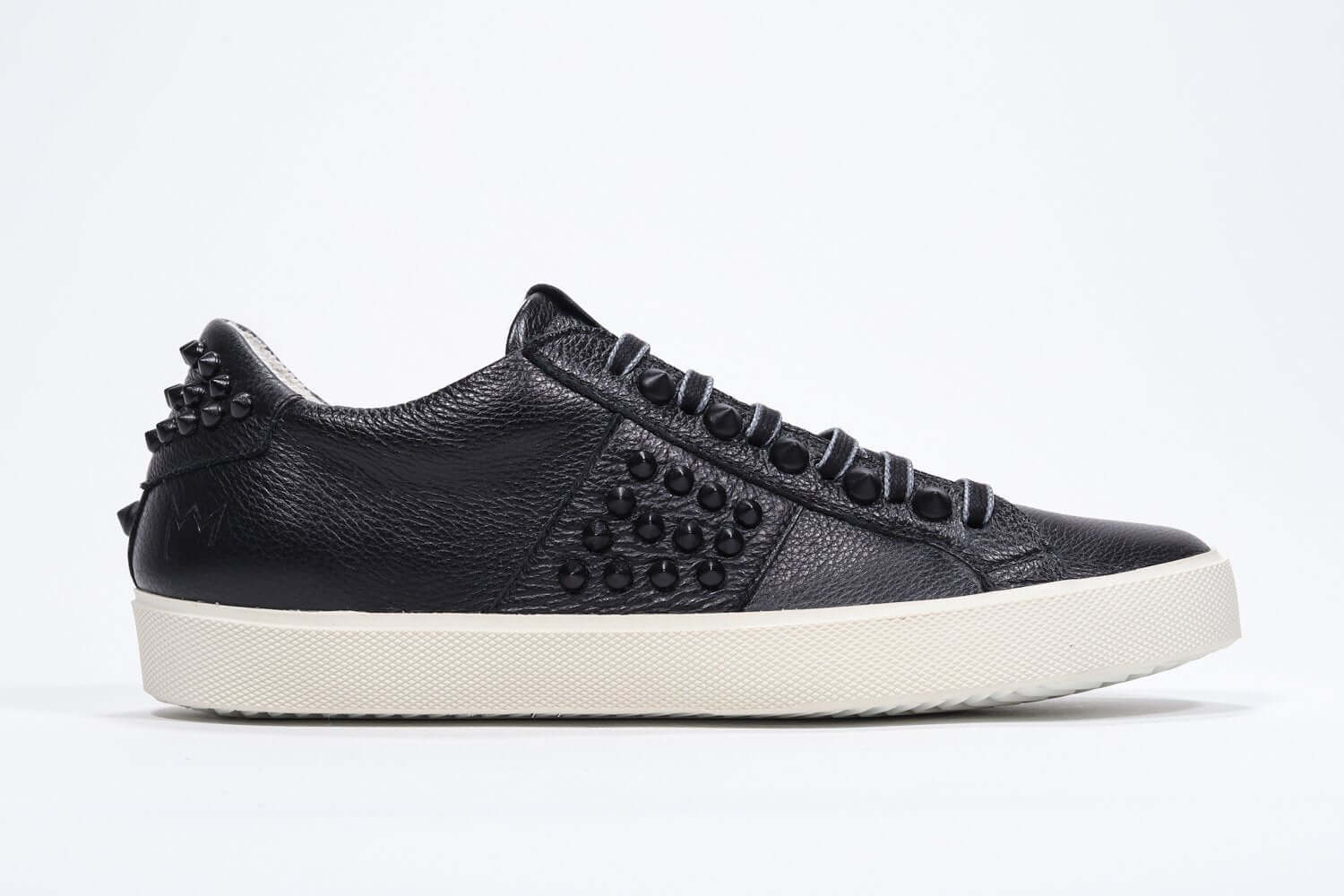 Side profile of low top black sneaker. Full leather upper with studs and vintage rubber sole.