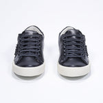 Front view of low top black sneaker. Full leather upper with studs and vintage rubber sole.