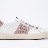 Side profile of low top white and pale pink sneaker. Full leather upper with studs and vintage rubber sole.