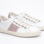 Three quarter front view of low top white and pale pink sneaker. Full leather upper with studs and vintage rubber sole.
