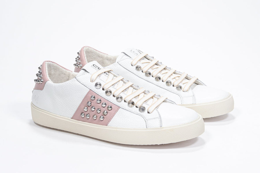 Three quarter front view of low top white and pale pink sneaker. Full leather upper with studs and vintage rubber sole.