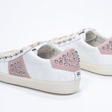 Three quarter back view of low top white and pale pink sneaker. Full leather upper with studs and vintage rubber sole.