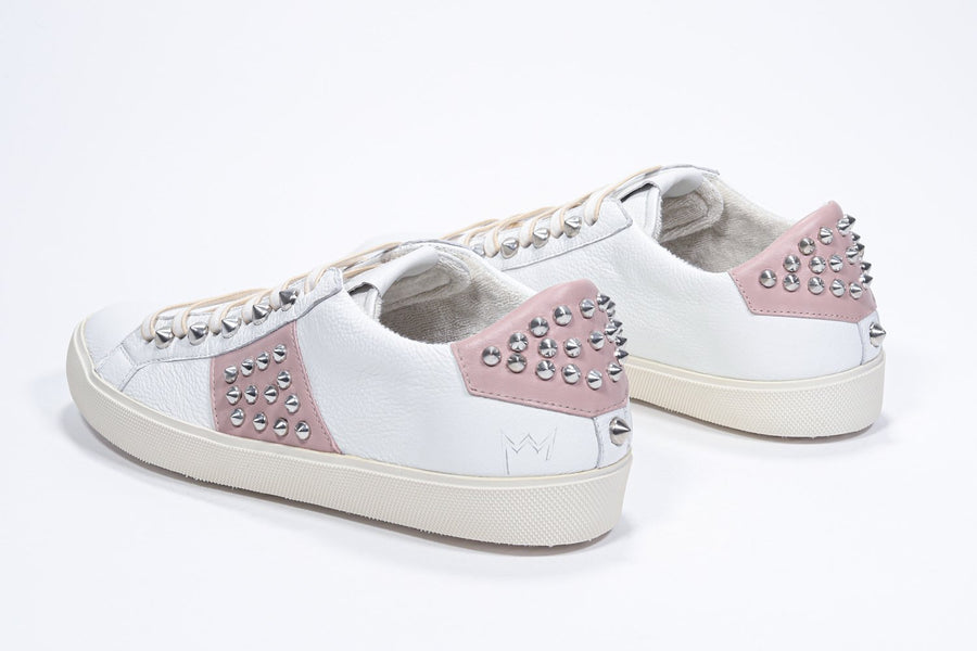 Three quarter back view of low top white and pale pink sneaker. Full leather upper with studs and vintage rubber sole.