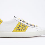 Side profile of low top white and yellow sneaker. Full leather upper with studs and white rubber sole.