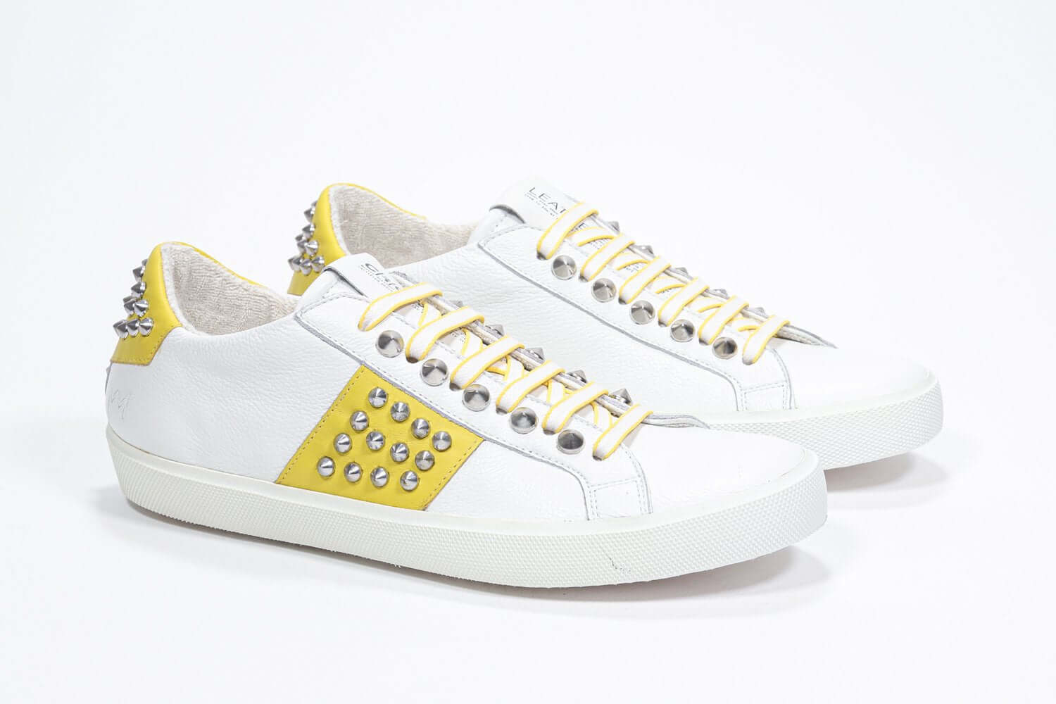Three quarter front view of low top white and yellow sneaker. Full leather upper with studs and white rubber sole.