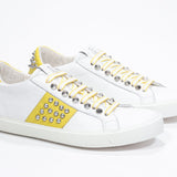 Three quarter front view of low top white and yellow sneaker. Full leather upper with studs and white rubber sole.