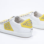 Three quarter back view of low top white and yellow sneaker. Full leather upper with studs and white rubber sole.