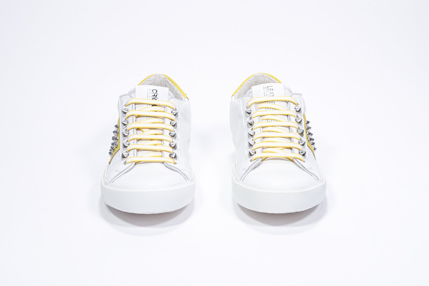 Front view of low top white and yellow sneaker. Full leather upper with studs and white rubber sole.